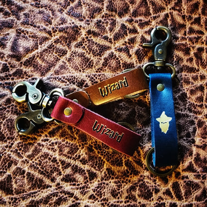 Handcrafted leather character class keychain with hand-gilded D&D class symbols and steel hardware for FLGS point of purchase retail counter displays.